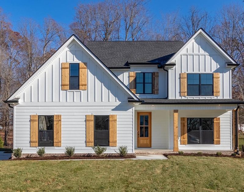 A white two-story home with board and batten siding on the second floor and plank siding on the first. It features light natural wood shutters.