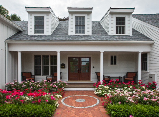 Cape-Cod-Style-House-With-White-HardiePlank-Lap-Siding-And-Red-Pink-White-Flower-Garden