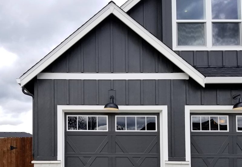 A garage featuring dark gray board and batten siding with white trim for a two-tone contrast look.