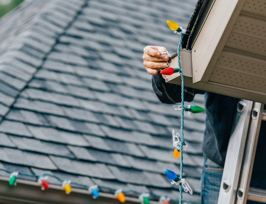 man on ladder hanging christmas lights outside