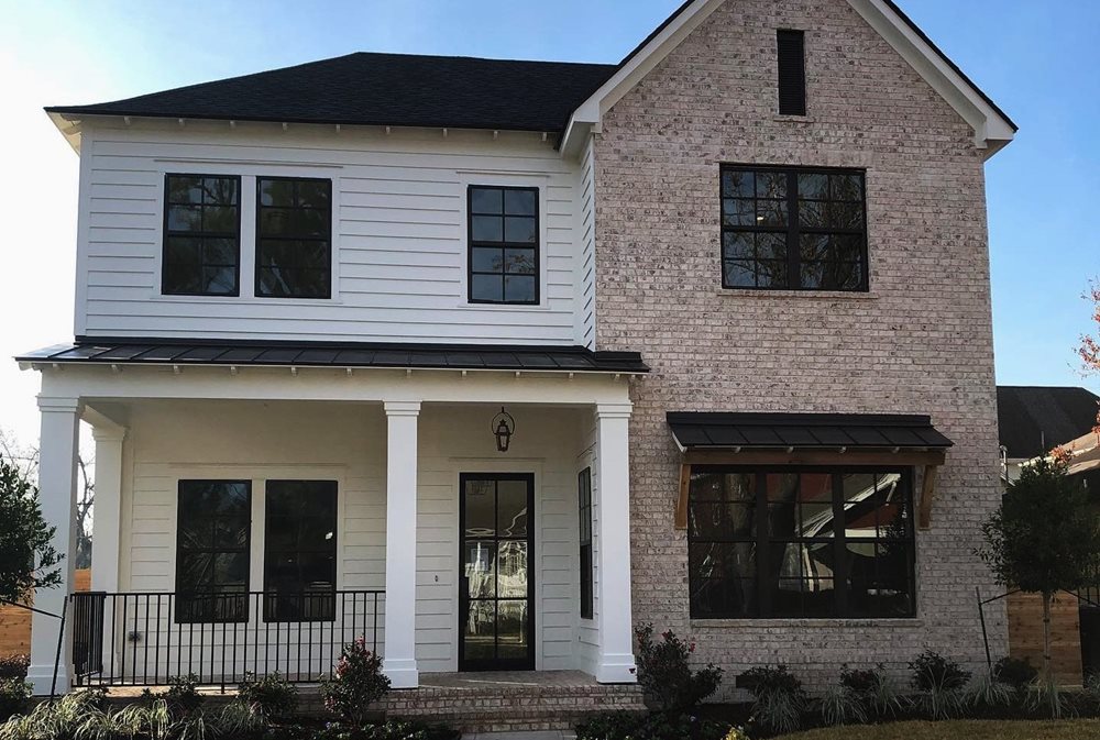 A neutral siding and stone color palette with white siding, red-ish brick and black windows.